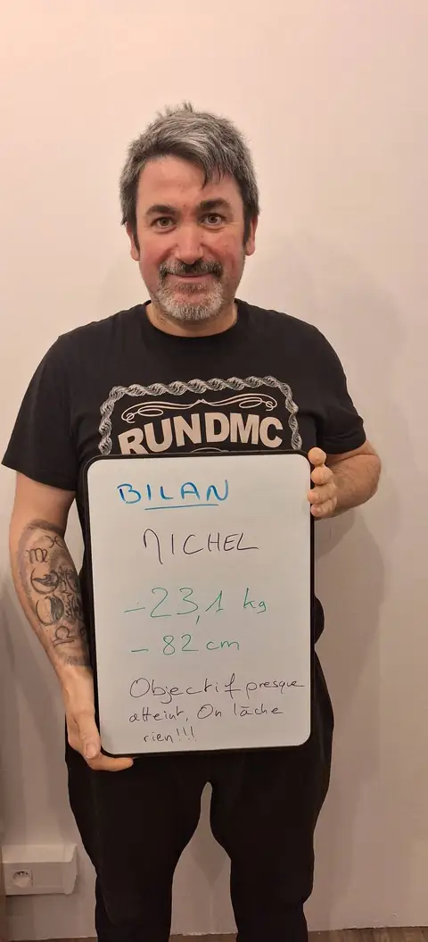 Un membre pose devant une ardoise blanche où sont notées ses mesures de bilan, au club
