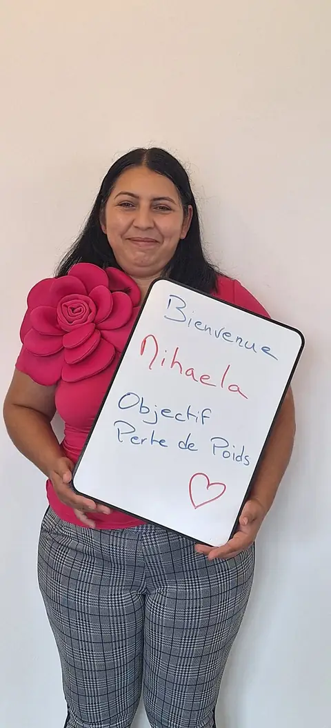 Une membre pose devant une ardoise blanche où sont notées ses mesures de bilan, au club