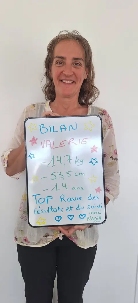 Une membre pose devant une ardoise blanche où sont notées ses mesures de bilan, au club