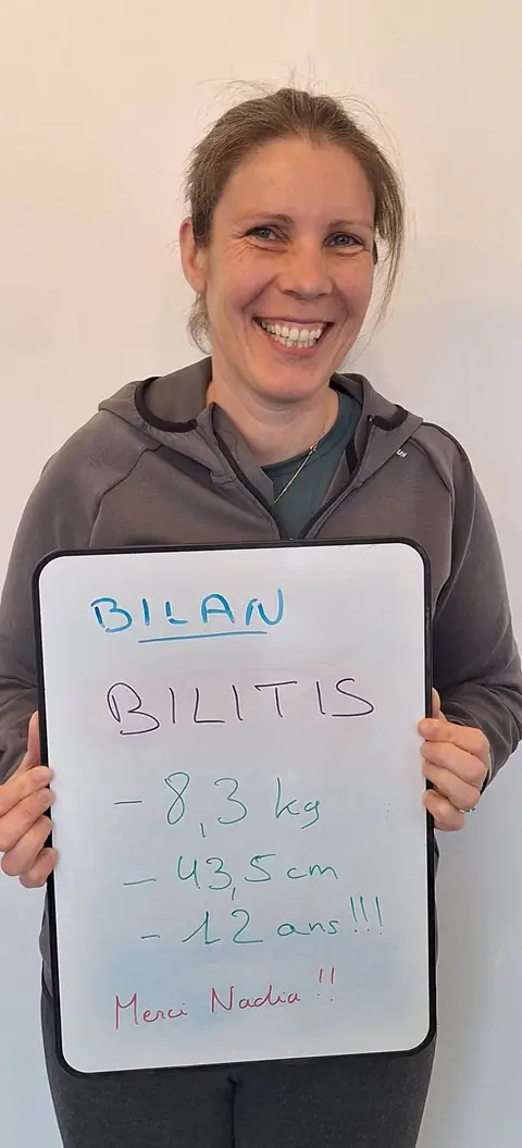 Une membre pose devant une ardoise blanche où sont notées ses mesures de bilan, au club